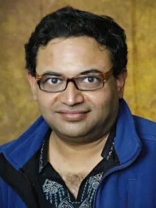 Andy De in blue jacket and glasses, casual portrait.