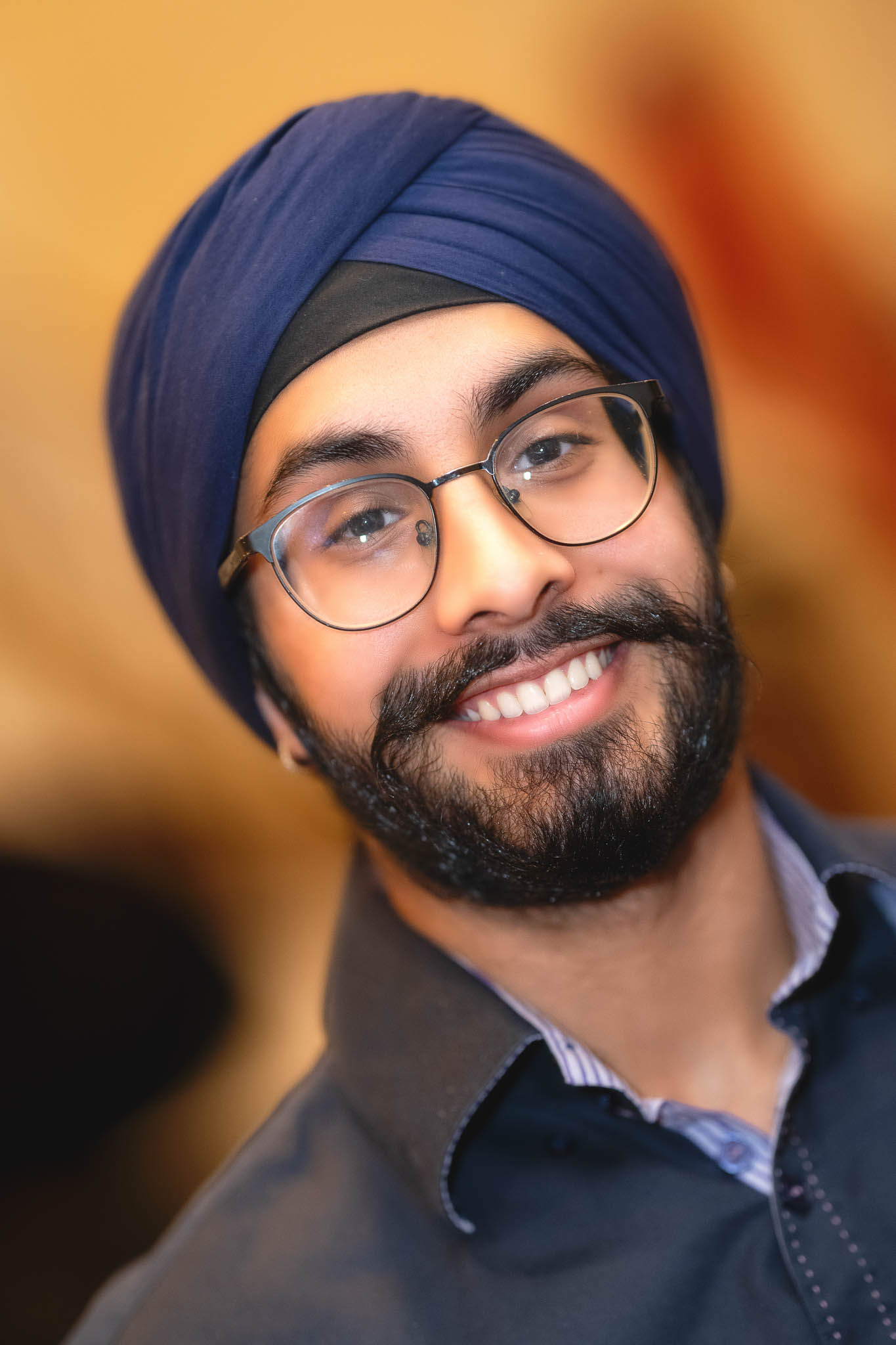 Smiling Sikh man in a navy turban and glasses indoors