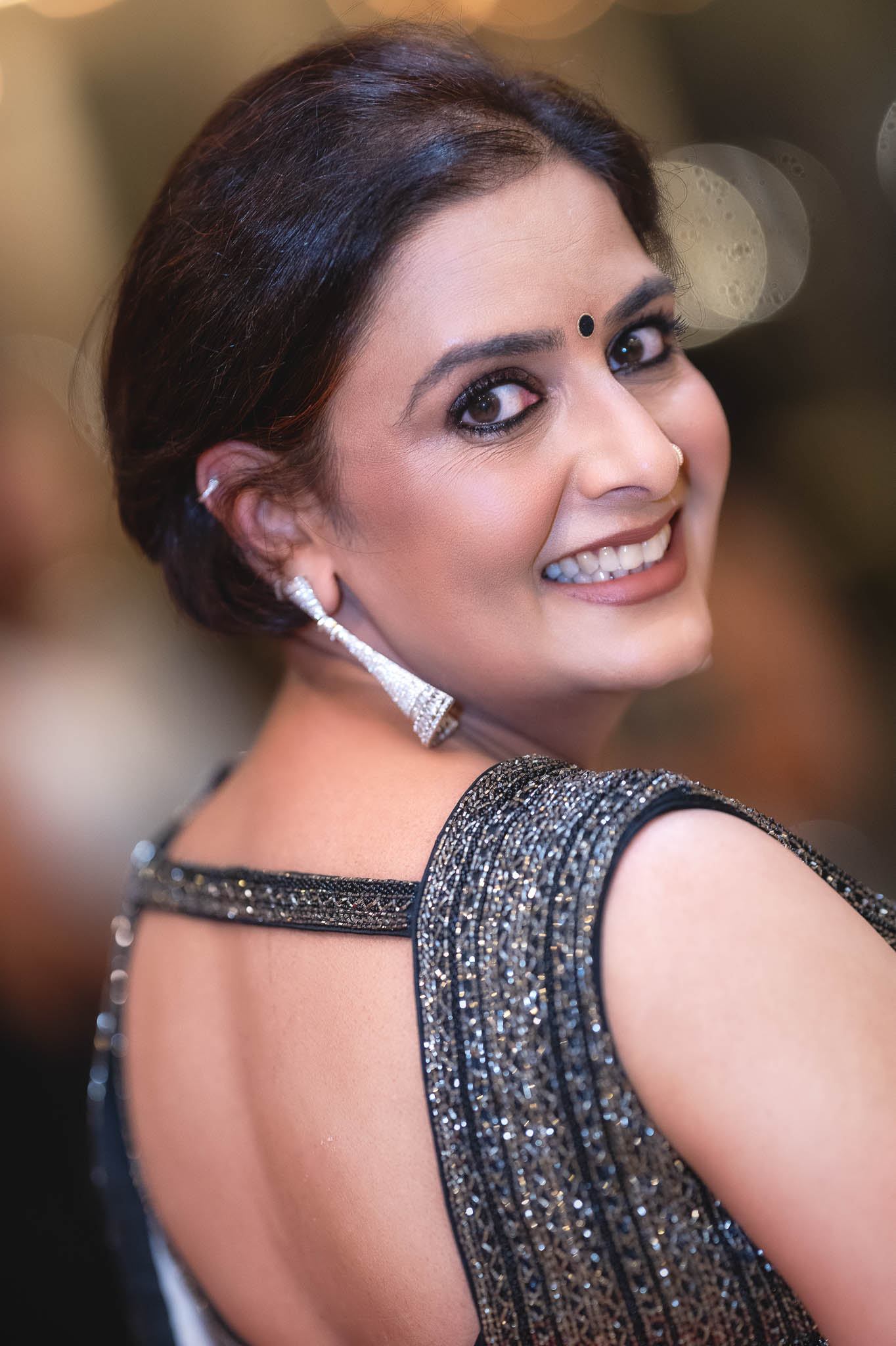 Smiling woman in a sparkling charcoal sari at an elegant indoor celebration.
